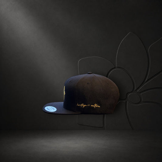 KA'EO Apparel black snapback cap with gold embroidery featuring a sampaguita flower and heritage + culture script.