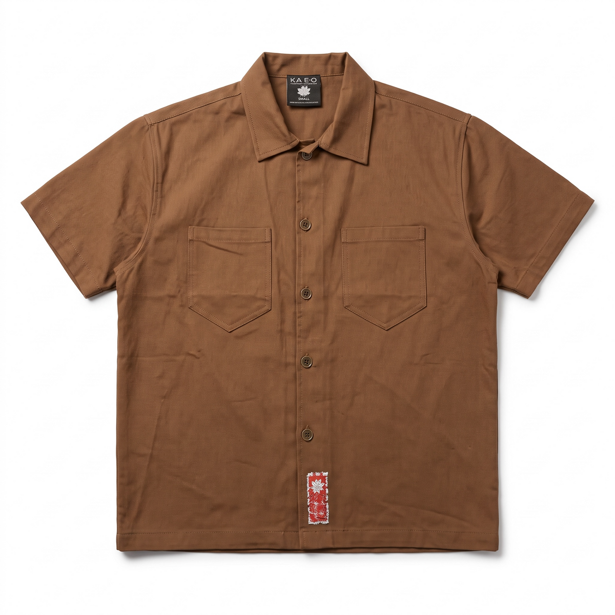 KA'EO Apparel brown short-sleeve cotton button-up shirt with dual chest pockets and a small woven label detail.