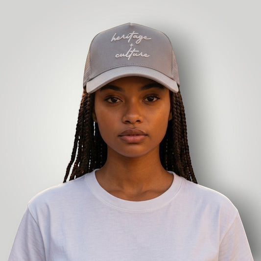 KA'EO Apparel gray cotton snapback cap with embroidered 'heritage + culture' script and curved brim, worn by a woman.