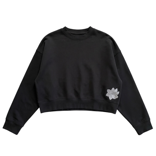 KA'EO Apparel black relaxed cropped fleece crewneck sweatshirt with embroidered Sampa flower detail on the hem.