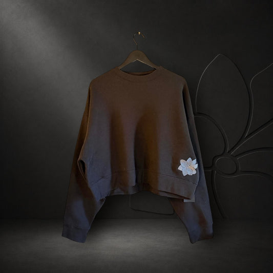 KA'EO Apparel black relaxed cropped fleece crewneck sweatshirt with embroidered Sampa flower detail on the hem.