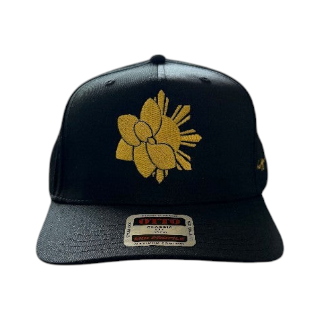 KA'EO Apparel black snapback cap featuring gold Sampa-Sol symbol embroidery and heritage script on a dark background.