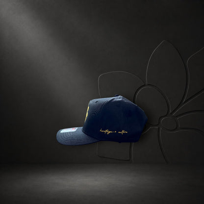 KA'EO Apparel navy blue snapback cap with gold Sampa-Sol embroidery and heritage + culture script on the side.