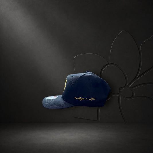 KA'EO Apparel navy blue snapback cap with gold Sampa-Sol embroidery and heritage + culture script on the side.