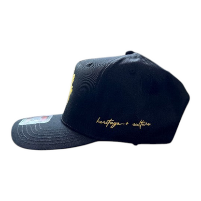 KA'EO Apparel navy blue snapback cap with gold Sampa-Sol embroidery and heritage + culture script on the side.