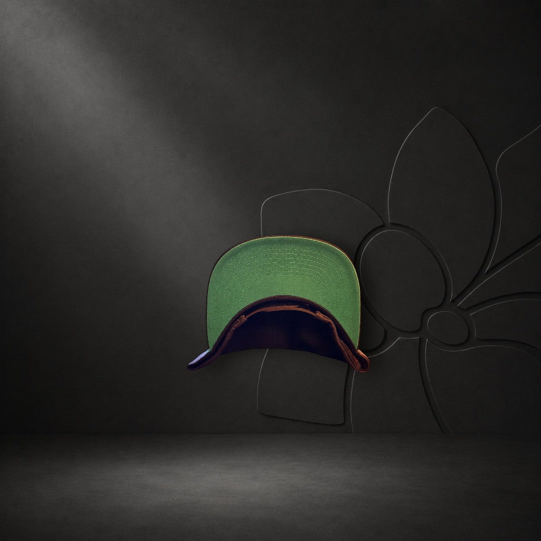 KA'EO Apparel black snapback cap with a contrasting green underbrim, displayed against a dark floral background.
