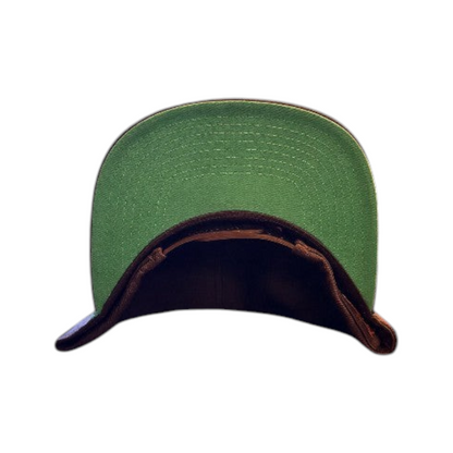 KA'EO Apparel black snapback cap with a contrasting green underbrim, displayed against a dark floral background.