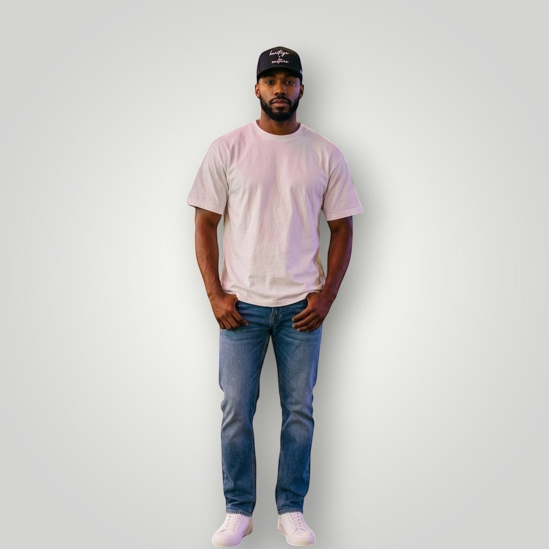KA'EO Apparel black cotton baseball cap with embroidered "heritage + culture" text and KA'EO logo on side. Model wears cap with white t-shirt and jeans.