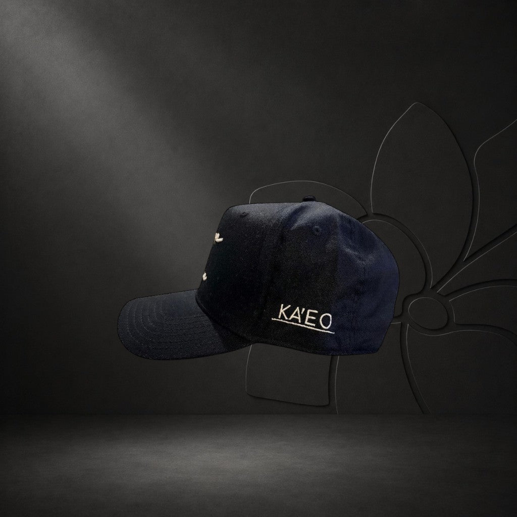 KA'EO Apparel black cotton baseball cap with embroidered "heritage + culture" script and side branding.