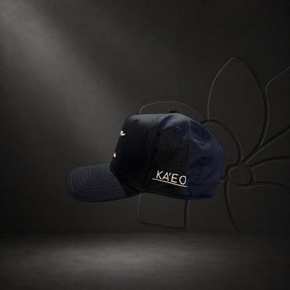 KA'EO Apparel black cotton baseball cap with embroidered "heritage + culture" script and side branding.