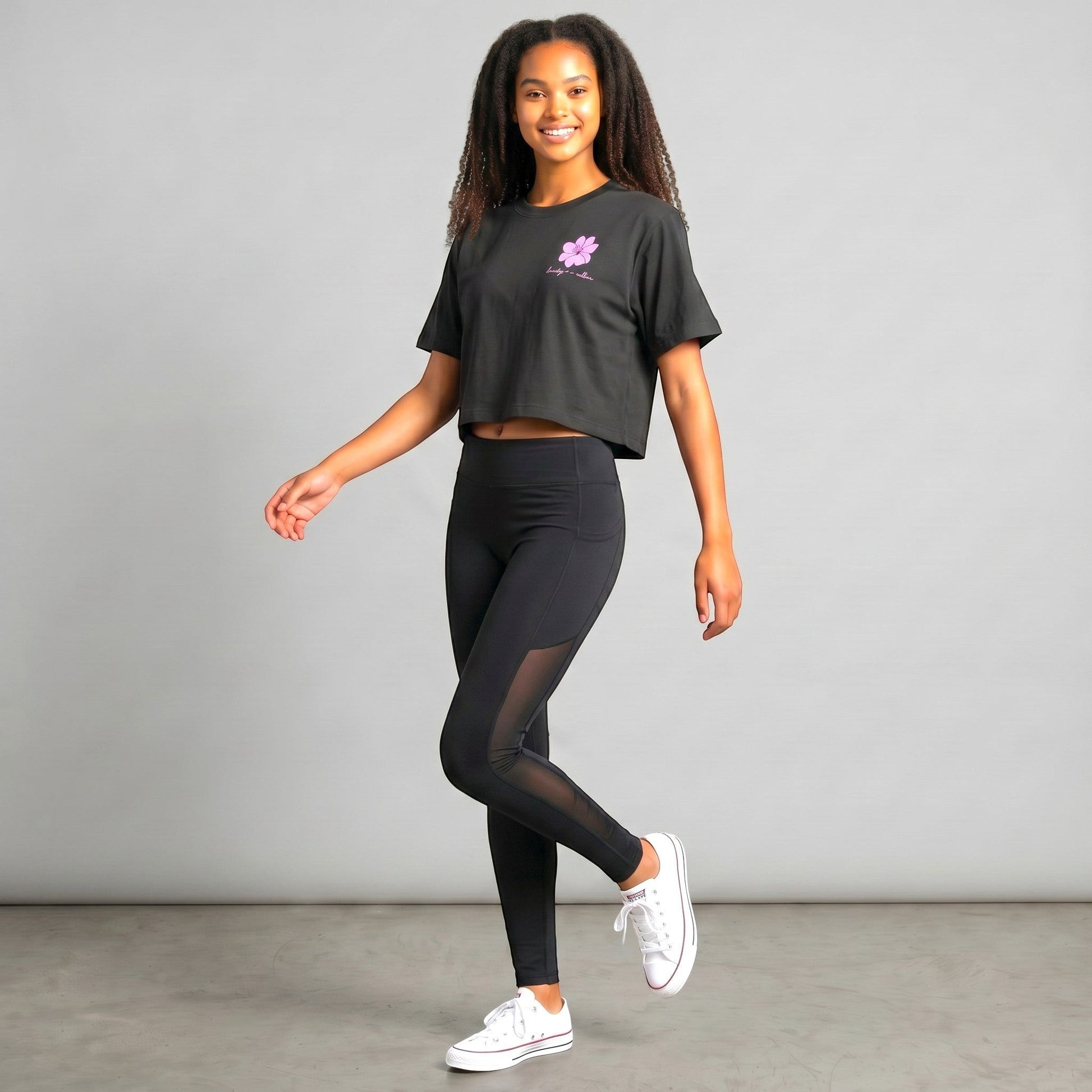 KA'EO Apparel black cropped t-shirt with pink Sampaguita graphic and script text. Model wears black leggings and white sneakers.