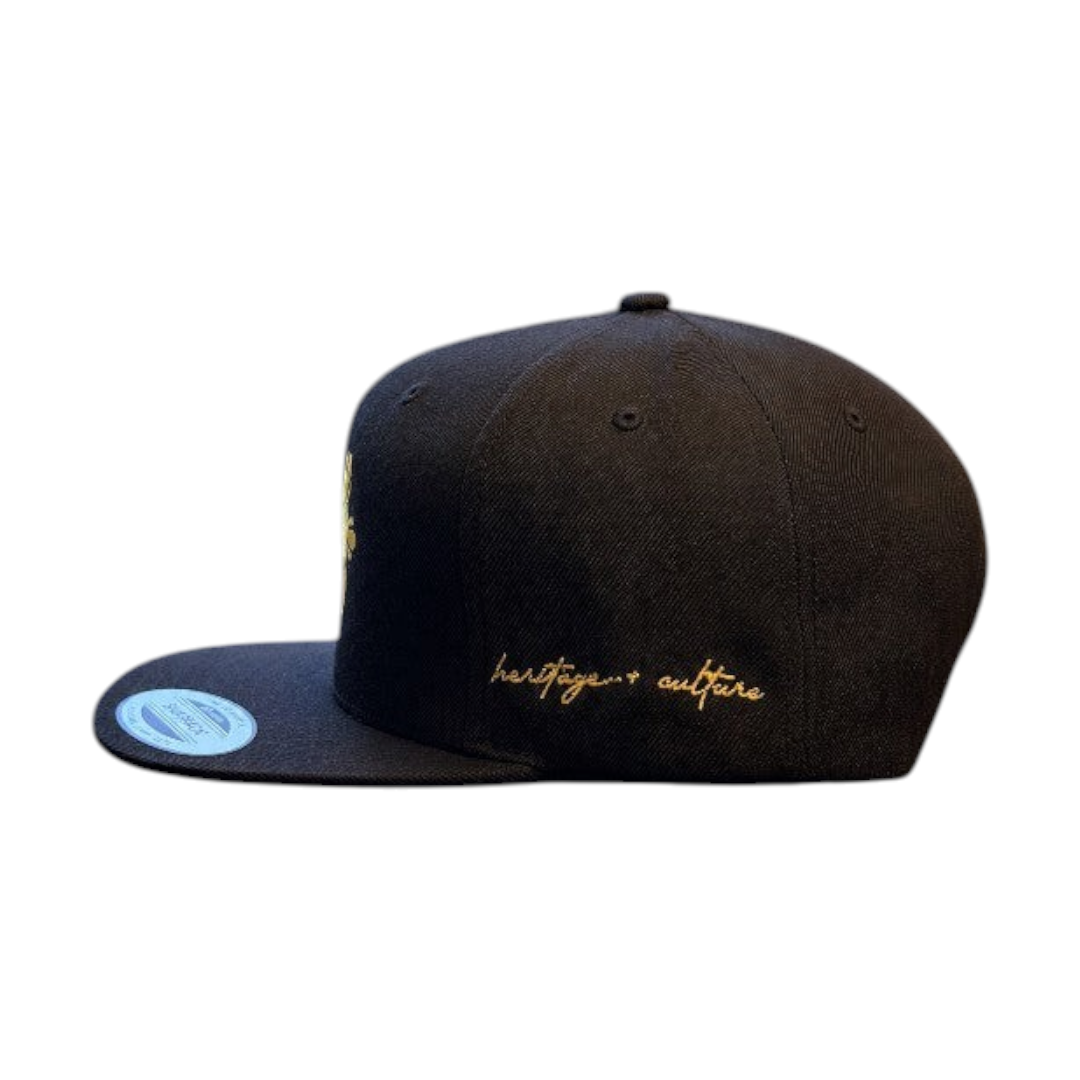 KA'EO Apparel black snapback cap with gold embroidery featuring a sampaguita flower and heritage + culture script.