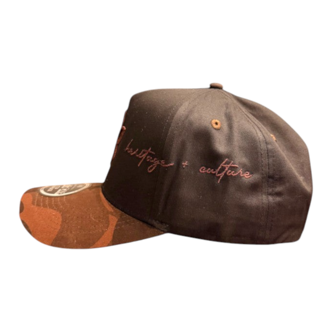 KA'EO Apparel brown snapback hat featuring a camo brim and embroidered heritage + culture text on the side panel.