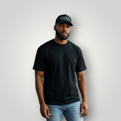 KA'EO Apparel dark grey trucker hat with embroidered logo and mesh back, worn by a man on a city street at night.