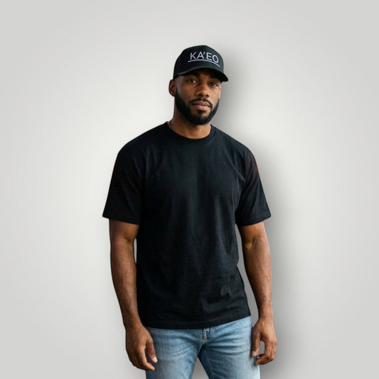 KA'EO Apparel dark grey trucker hat with embroidered logo and mesh back, worn by a man on a city street at night.