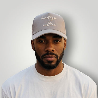 KA'EO Apparel gray cotton snapback cap with embroidered "heritage + culture" text and curved brim, worn by a man.