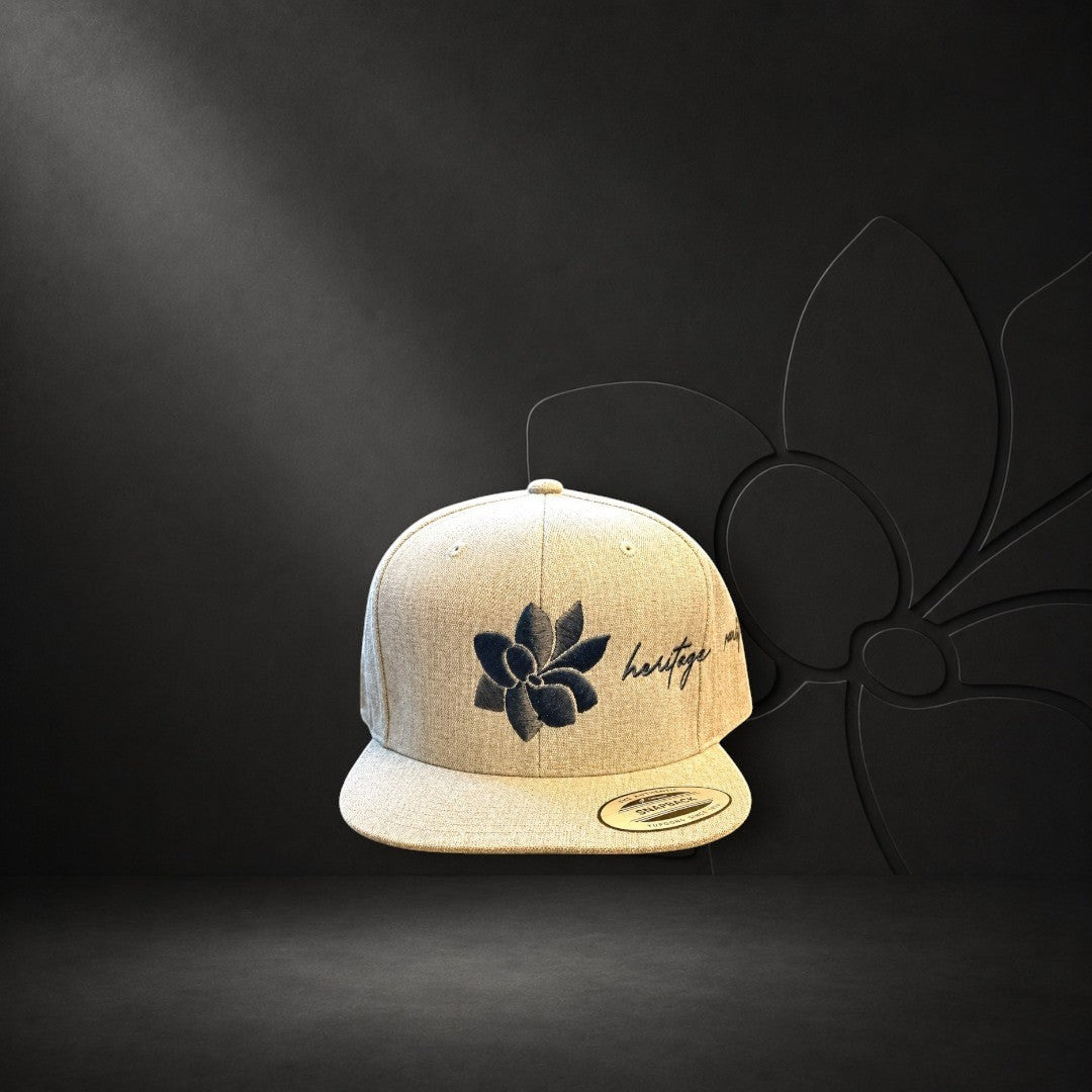 KA'EO Apparel heathered tan snapback hat with embroidered dark gray sampaguita flower and "heritage + culture" script.