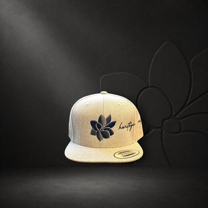 KA'EO Apparel heathered tan snapback hat with embroidered dark gray sampaguita flower and "heritage + culture" script.