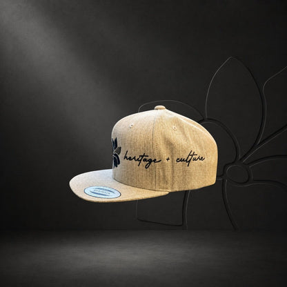 KA'EO Apparel heathered tan snapback hat with embroidered dark gray sampaguita flower and "heritage + culture" script.