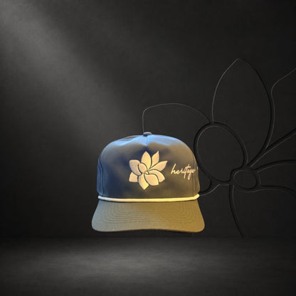KA'EO Apparel olive green baseball cap with white embroidered Sampaguita flower and "heritage" text. Features a cream rope detail